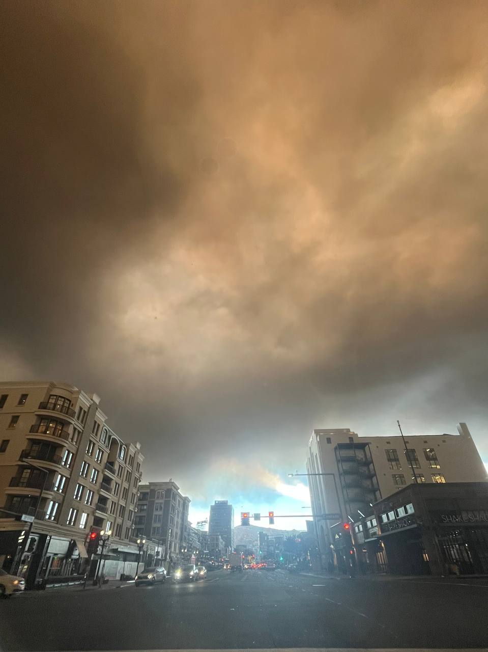 Orangeish gray smoke clouds cover most of the sky above a city street intersection.