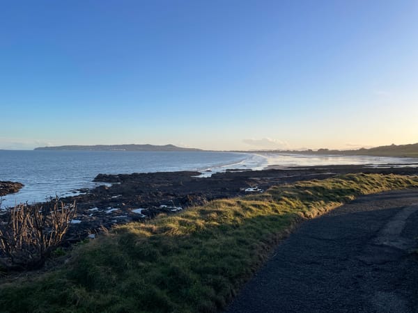 Irish Sea coastline with lots of rocks and Howth in the distance. A footpath in the foreground. 